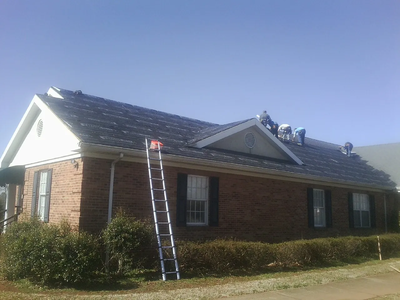 Crew tearing shingles off a brick ranch roof with a ladder set — Metal Roof Repair work by our crew in Selinsgrove