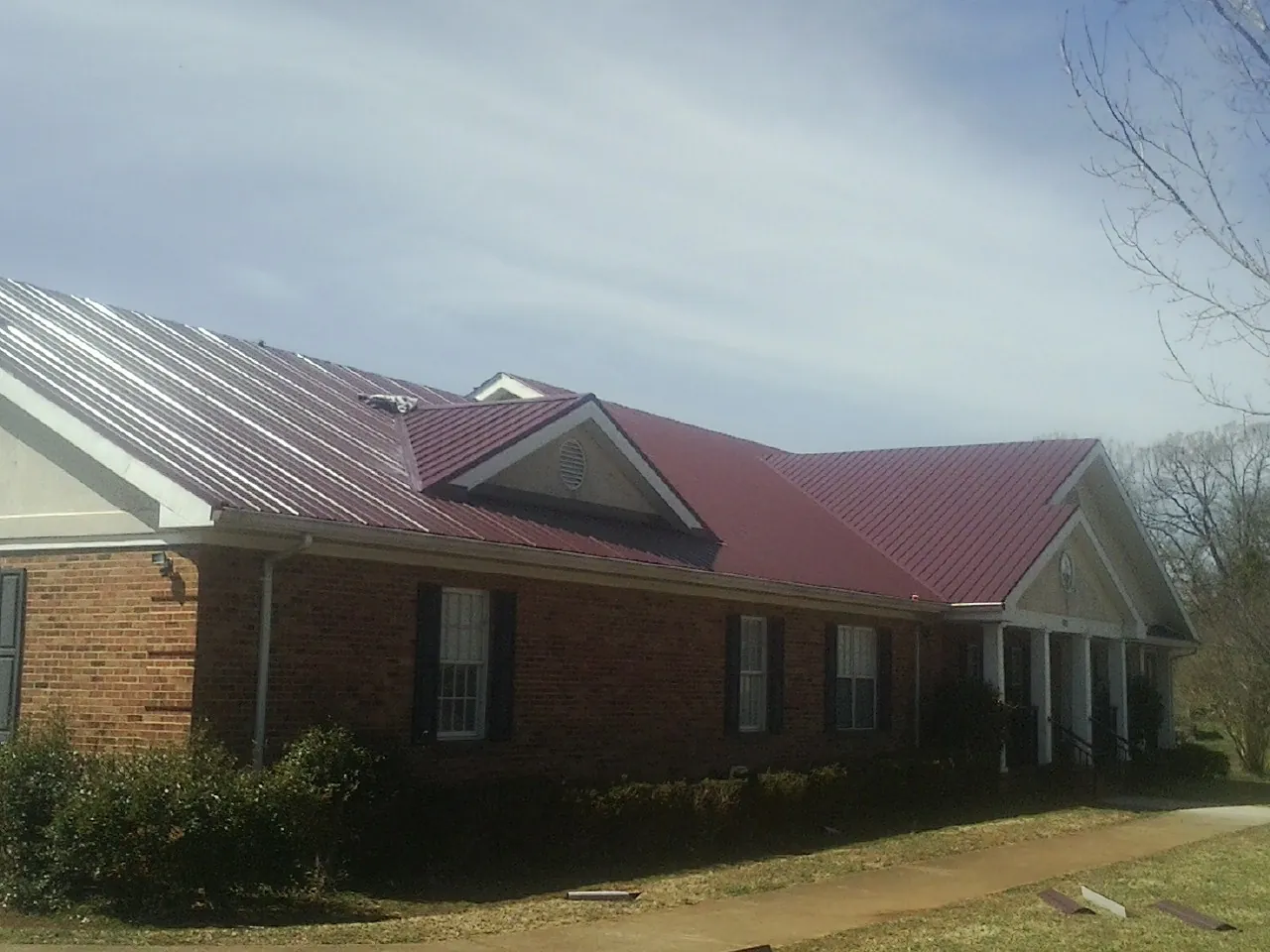 Red metal roof with gabled entries on a long brick building, from a Hail Damage Roof Repair job in Selinsgrove