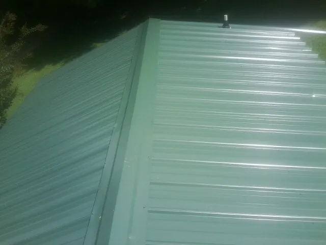 New green metal panels meeting at the ridge of a roof — Flat Roof Repair work by our crew in Selinsgrove
