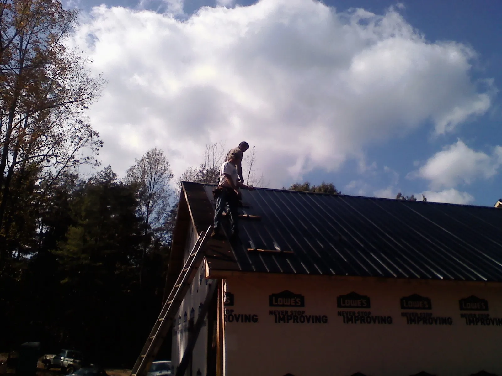 Roofer fastening dark metal panels high against a cloudy sky, from a Roof Inspection job in Selinsgrove