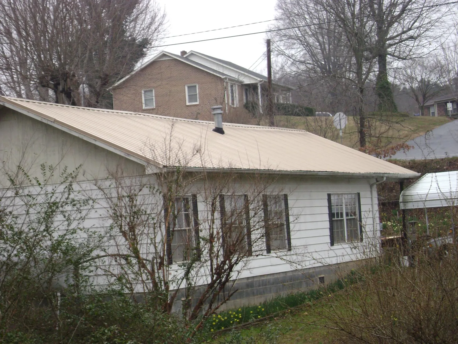 Tan metal roof on a white sided house set into a hillside — Commercial Roofing by Roofing Brothers in Selinsgrove